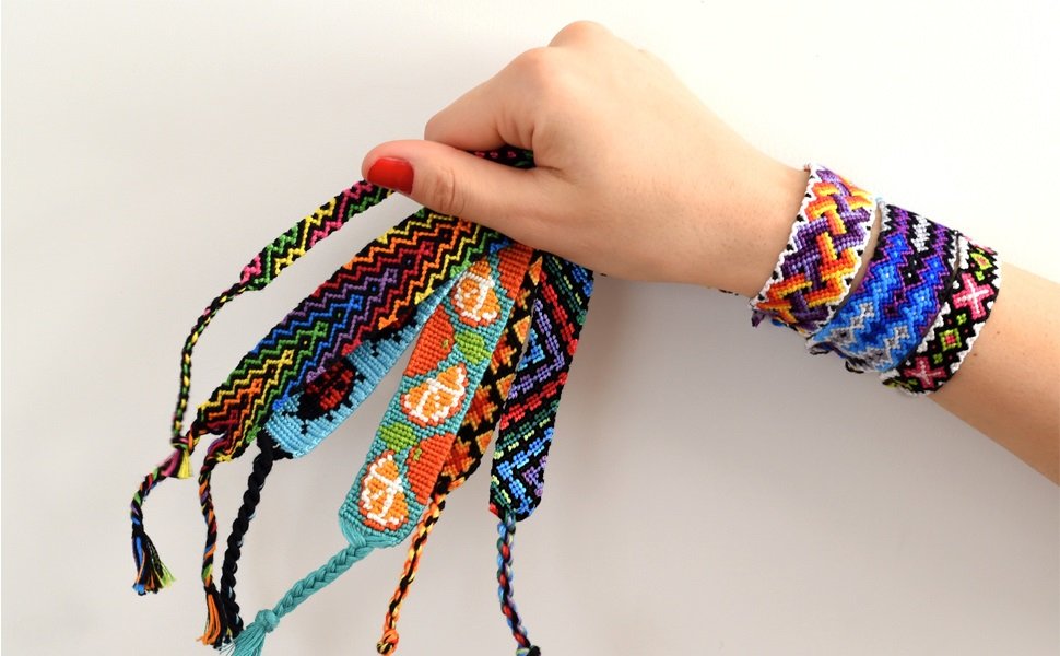 Hand holding colorful woven friendship bracelets with patterns including zigzags, ladybugs, and flowers. Several bracelets are worn on a wrist.