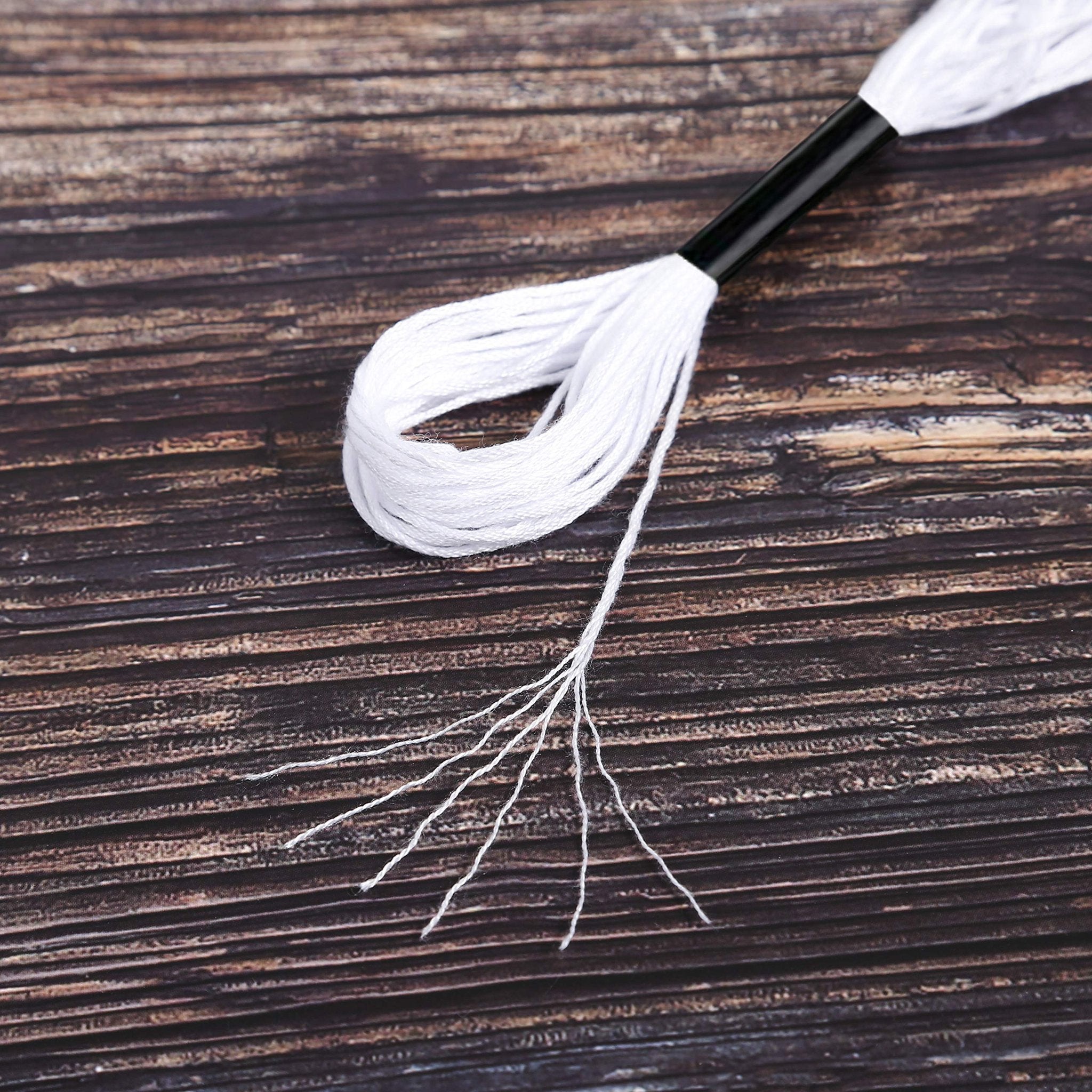 Close-up of white embroidery floss on a dark wooden background, with the floss partially wound and some strands frayed.