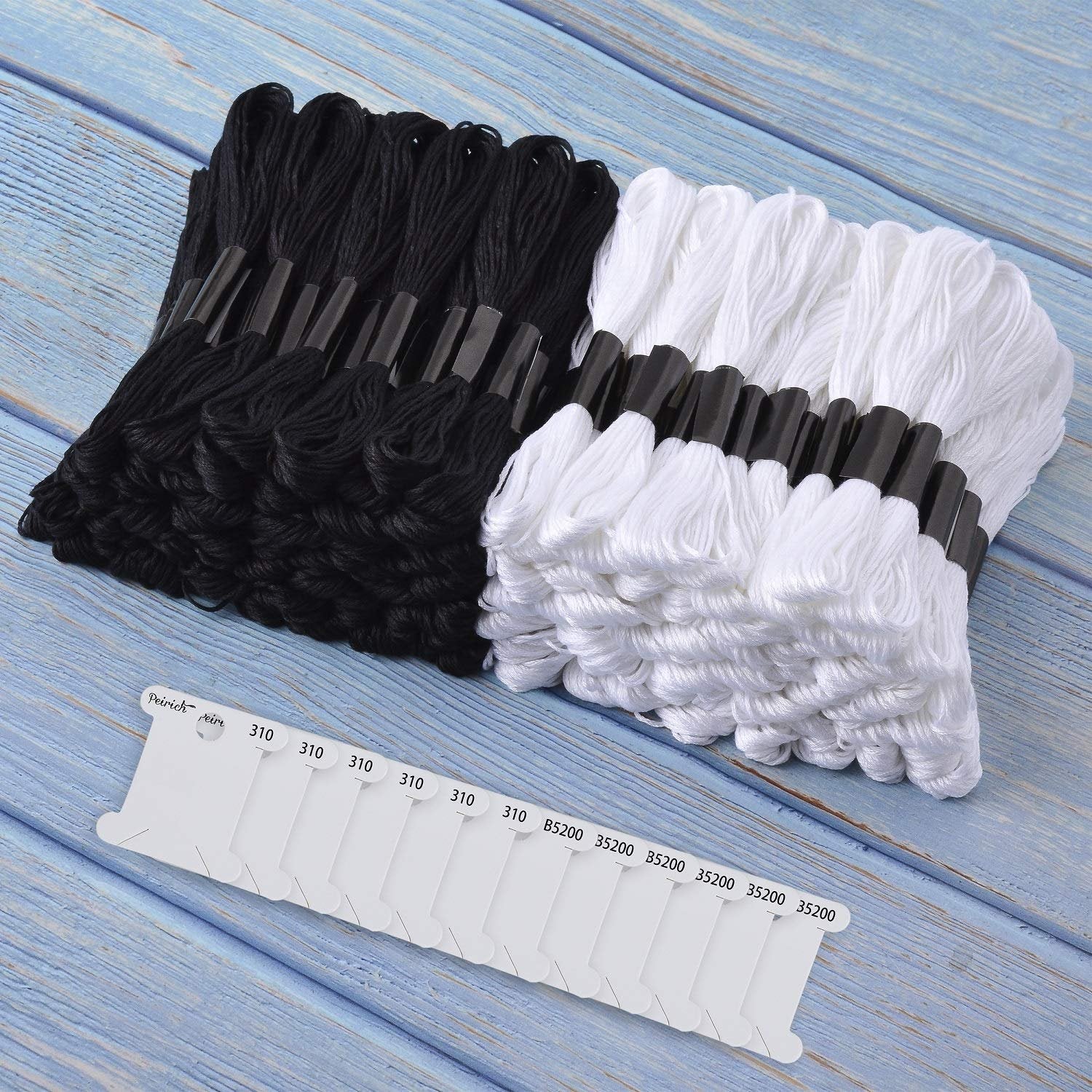 Black and white embroidery floss skeins arranged on a blue wooden surface with floss bobbins in the foreground.