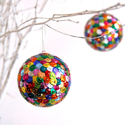 Two colorful sequin-covered spheres hanging from white branches against a white background.