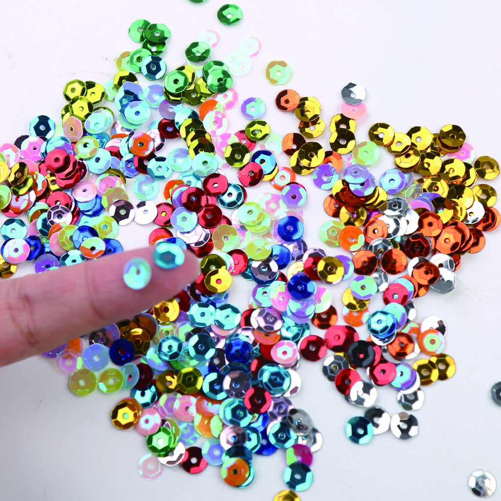 A finger holding a blue sequin above a pile of colorful 6mm round cup sequins for DIY crafts.