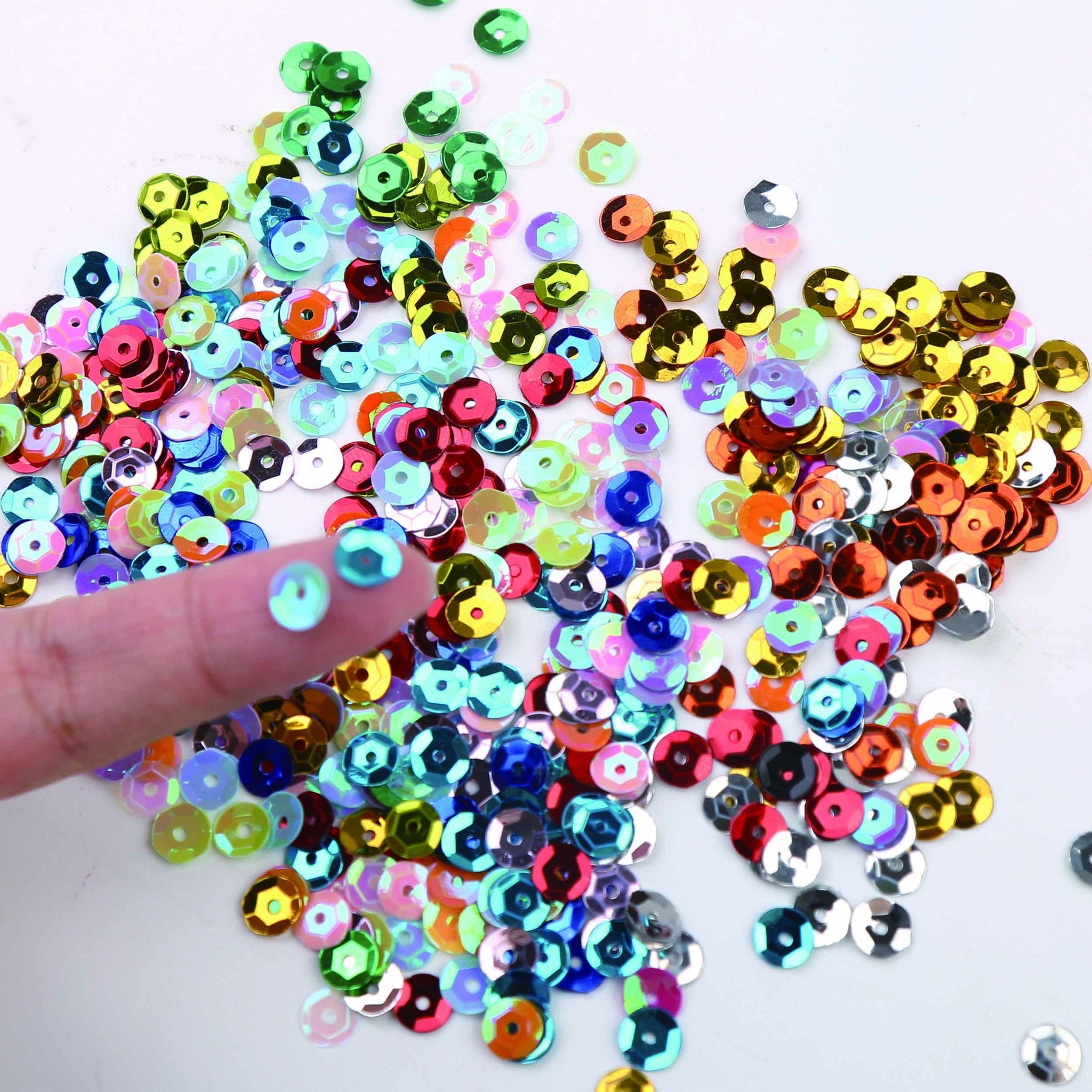 A finger holding a blue sequin above a pile of colorful 6mm round cup sequins for DIY crafts.