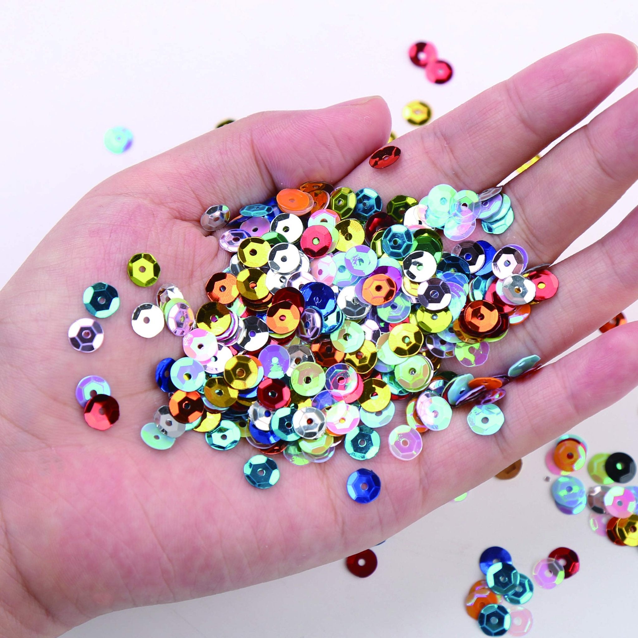 Hand holding a pile of colorful, round cup sequins with holes in various shades of red, blue, green, yellow, and orange.
