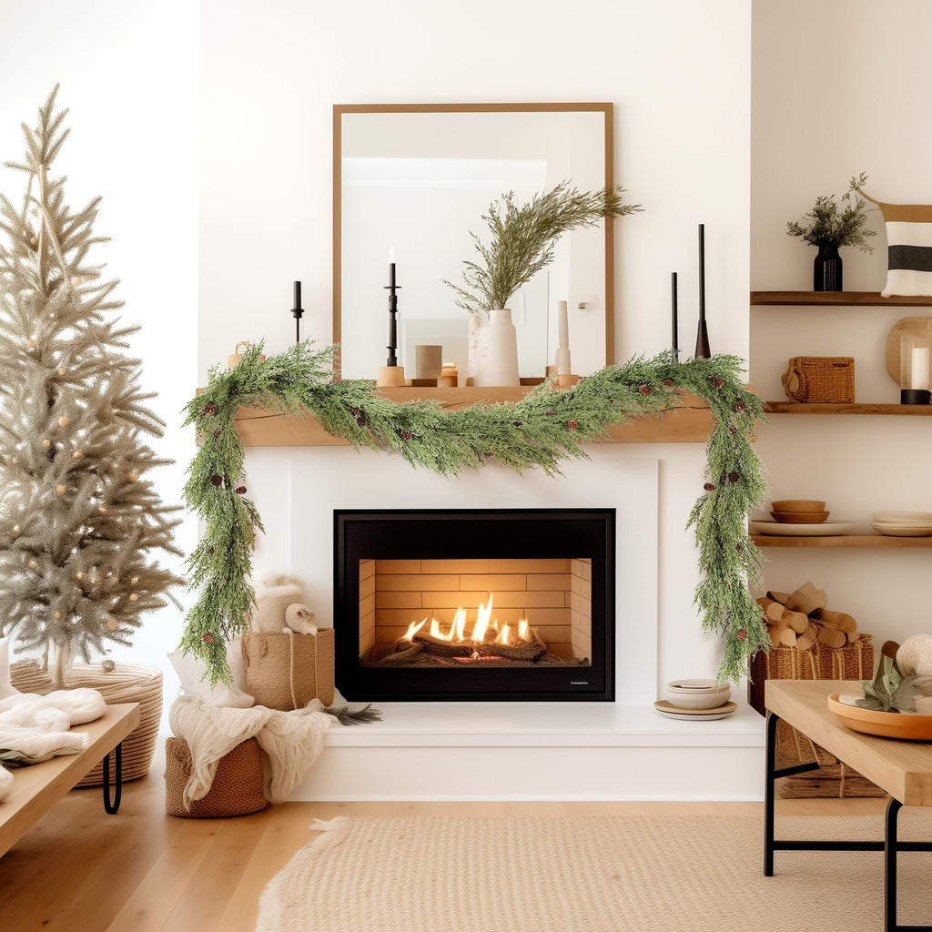 Christmas garland with pine cones draped over a fireplace mantel with a lit fire and a decorated tree nearby.