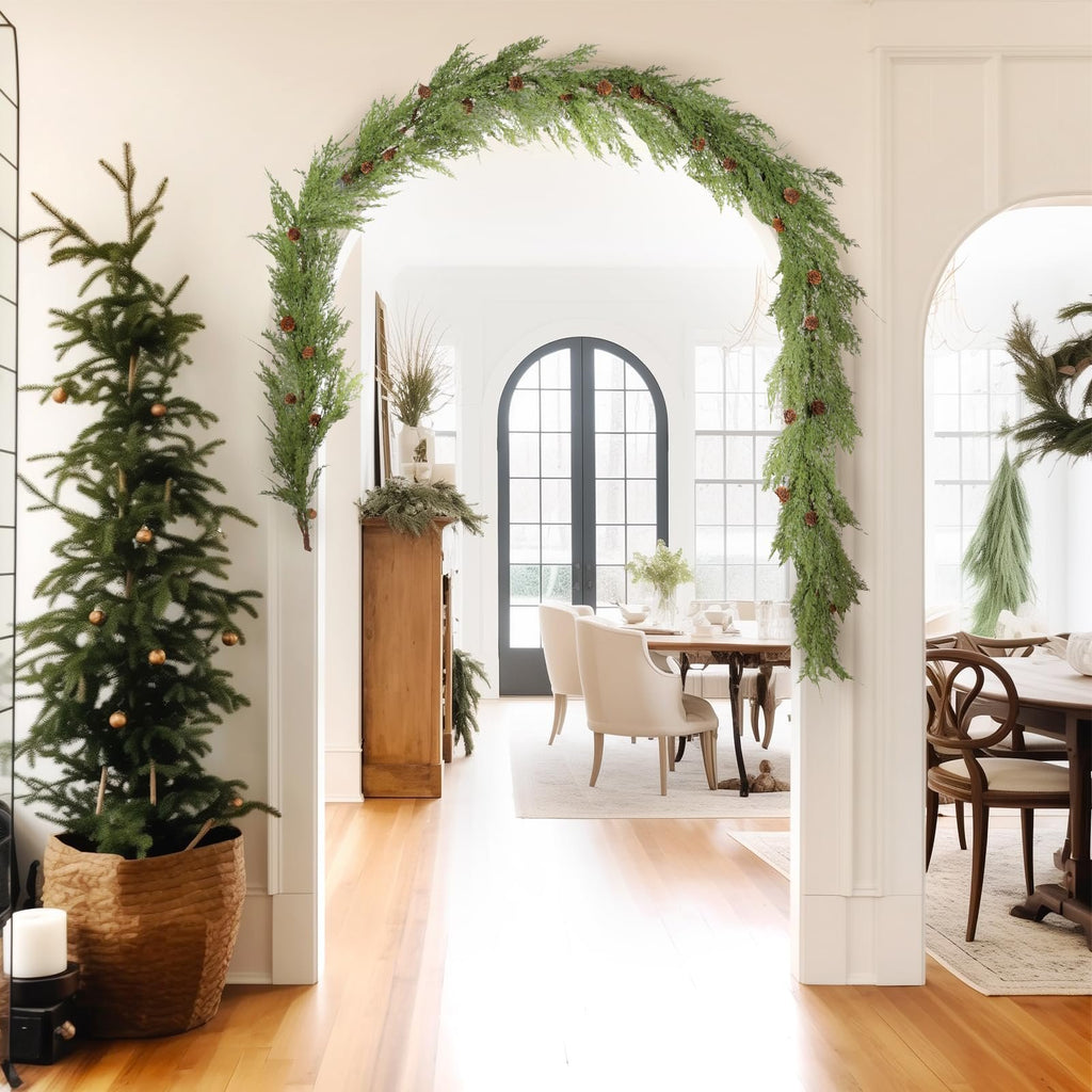 Christmas garland with pine cones draped over an archway, with a small decorated tree to the left and a dining room visible beyond.