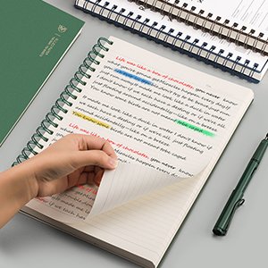 A5 college ruled notebook with green hardcover, open to pages with handwritten text and colorful highlights, and a green pen.