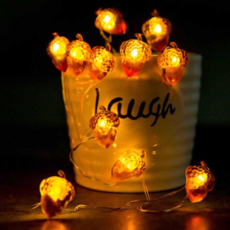Acorn-shaped string lights with warm LEDs draped around a white mug with the word 'laugh' visible.