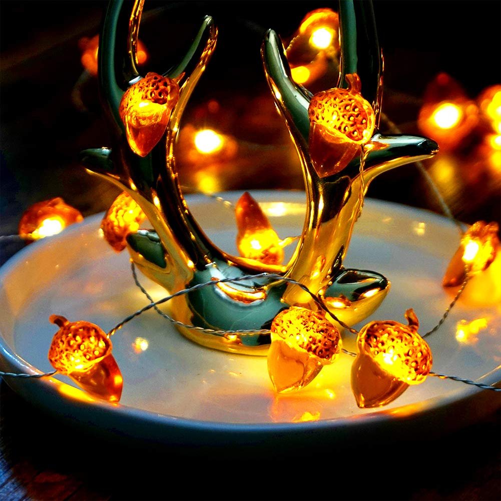 Acorn-shaped fairy string lights with warm LED bulbs draped around a gold deer antler decoration on a white plate.