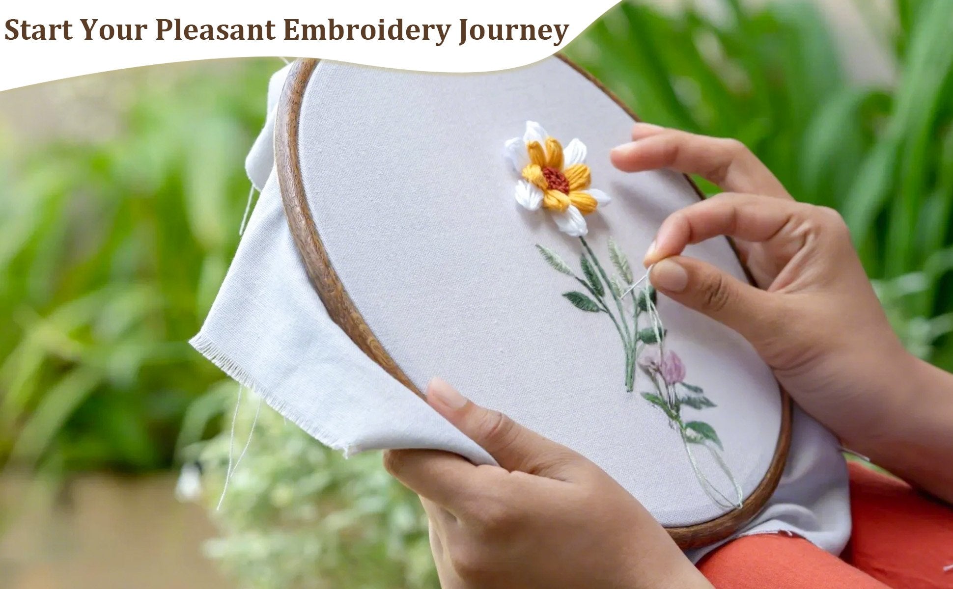Hands embroidering a floral design on fabric within a wooden hoop, with green foliage in the background.