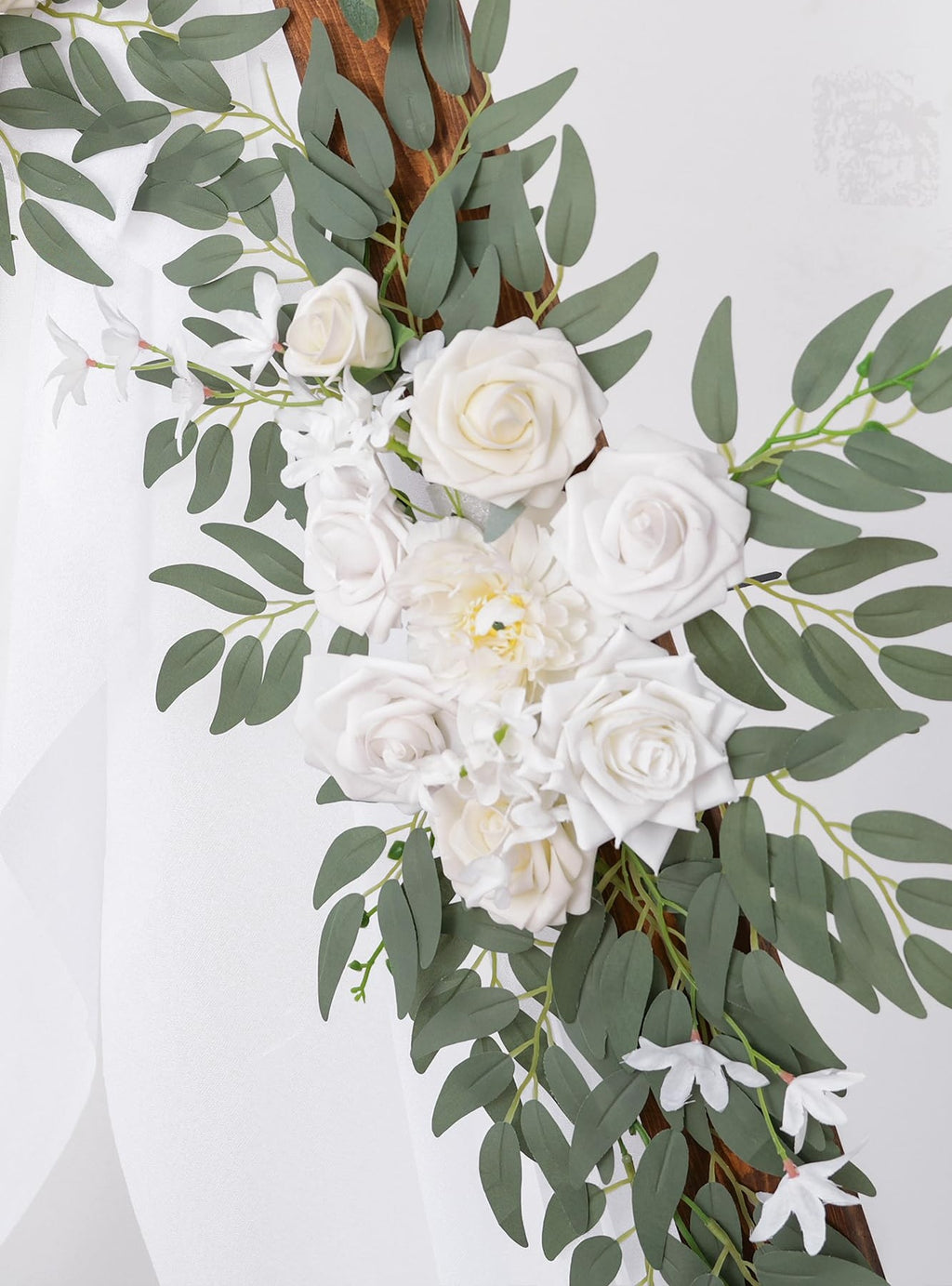 Wedding arch flower garland with white roses and eucalyptus leaves on a wooden frame, with sheer white fabric draped.