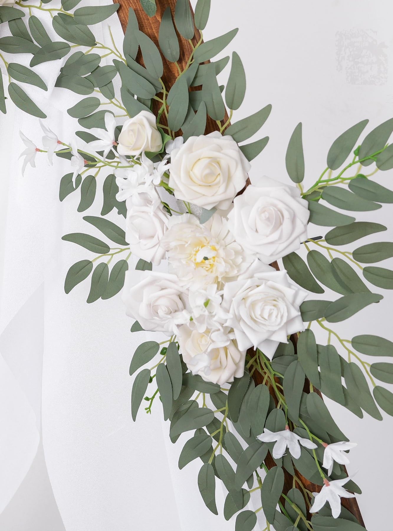 Wedding arch flower garland with white roses and eucalyptus leaves on a wooden frame, with sheer white fabric draped.
