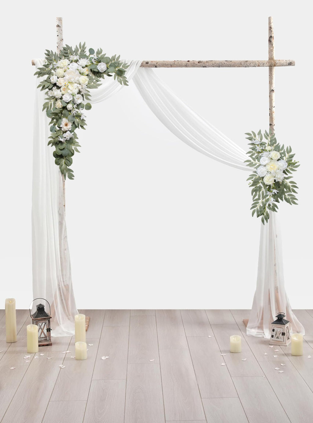 Wedding arch with floral garlands and draped fabric, set against a white background with candles and lanterns on a wooden floor.