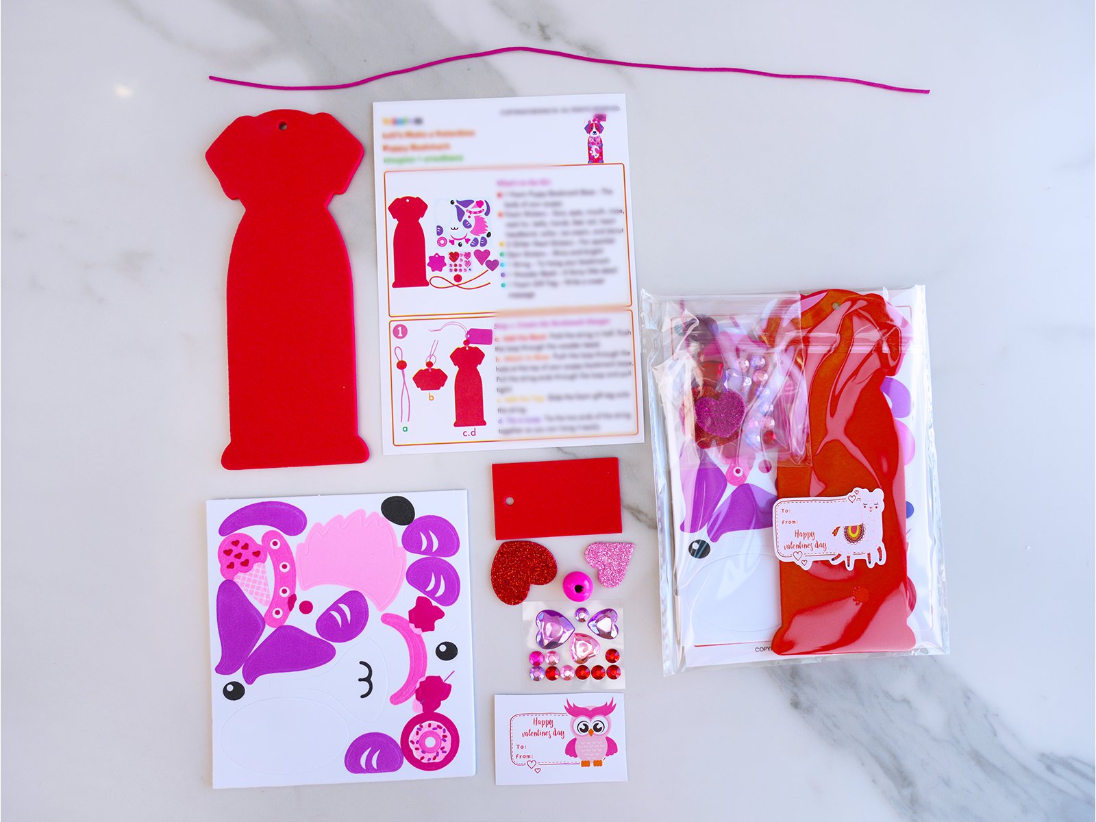 Craft kit contents including red dress-shaped cutout, foam stickers, gems, and instructions on a marble surface.