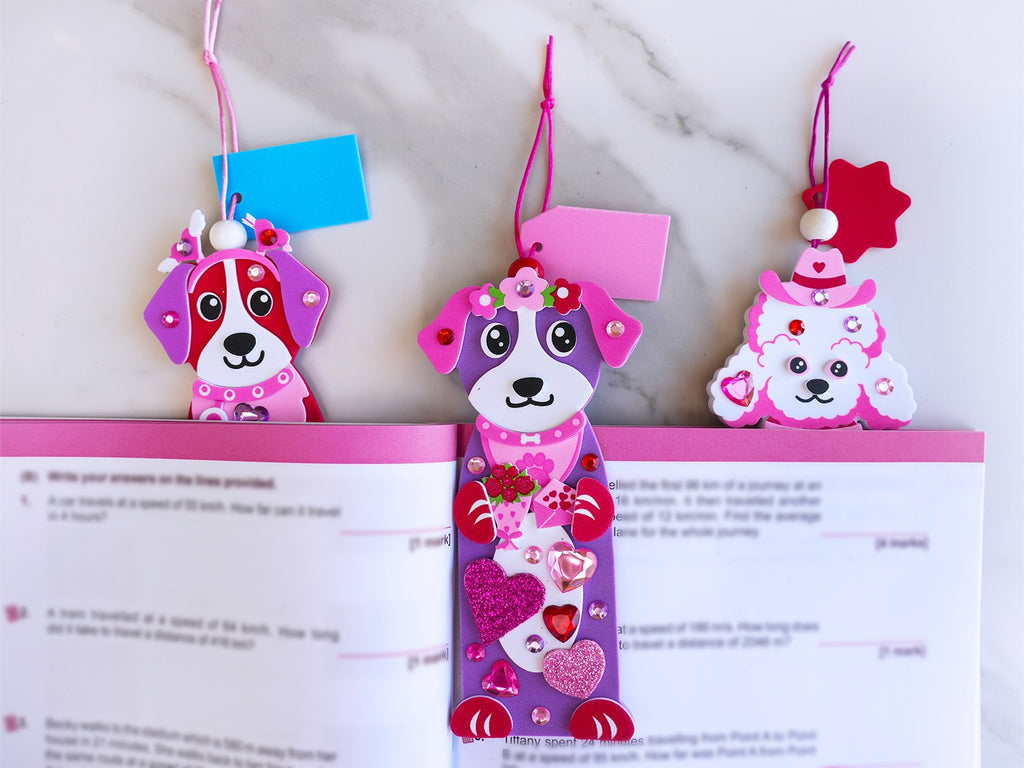 Three decorative dog-shaped bookmarks with rhinestones and hearts, placed in an open book.