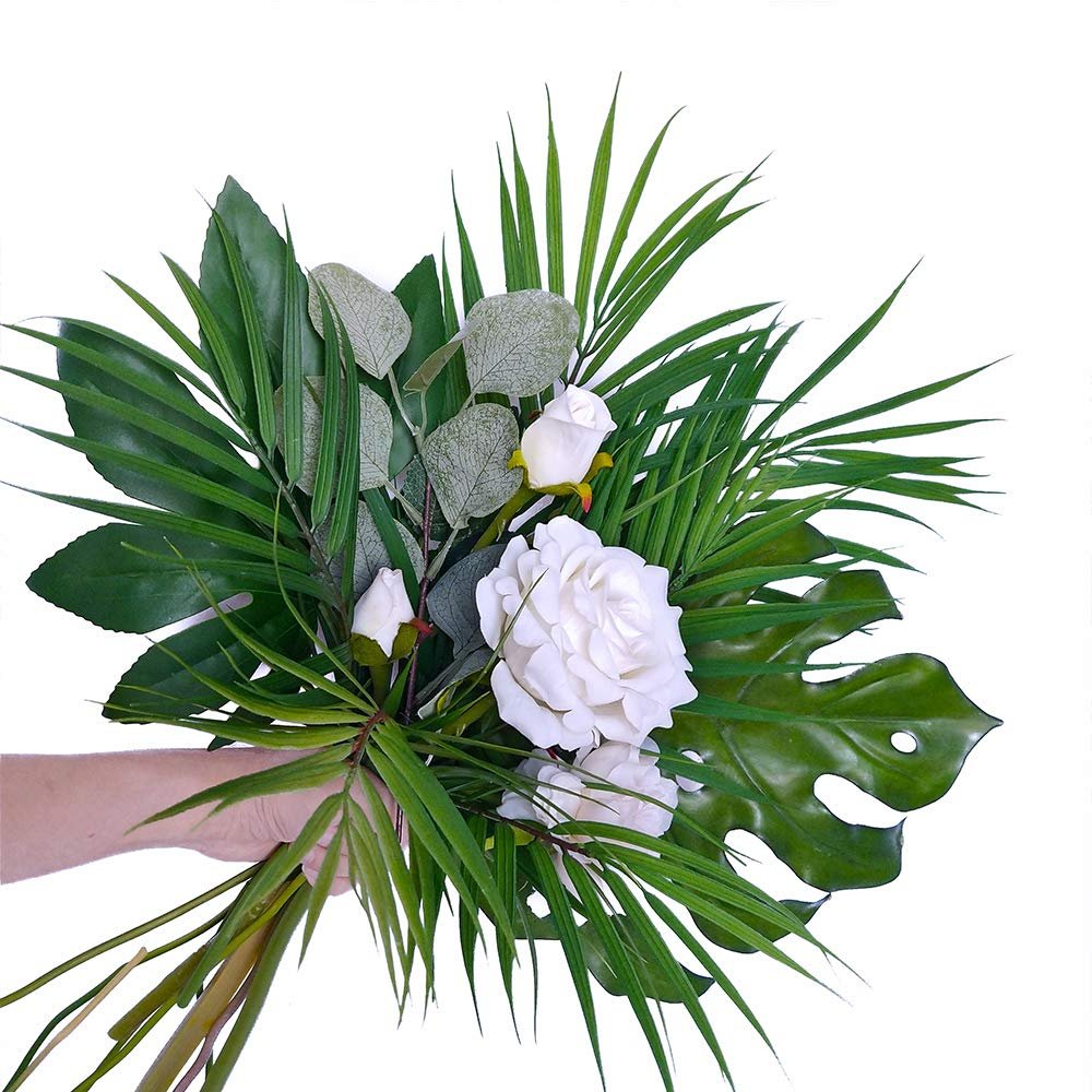 Hand holding artificial areca palm leaves and white roses bouquet against a white background