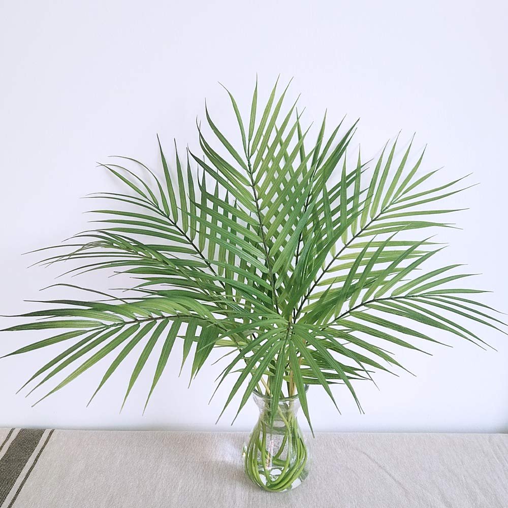 Artificial areca palm leaves in a glass vase on a table with a striped cloth