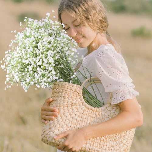 Woman holding a woven basket filled with white artificial baby's breath flowers in a field