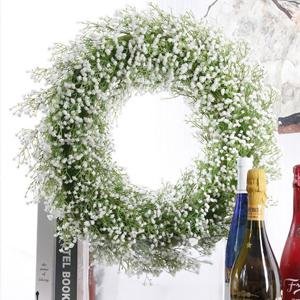 White artificial baby's breath wreath with green stems, displayed with bottles and books.