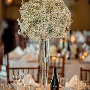 Tall glass vase filled with white baby's breath flowers on a decorated table at a wedding reception.
