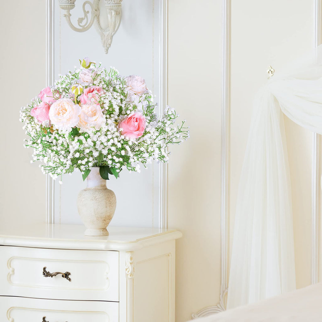 Bouquet of artificial pink and white roses with baby's breath in a textured vase on a dresser