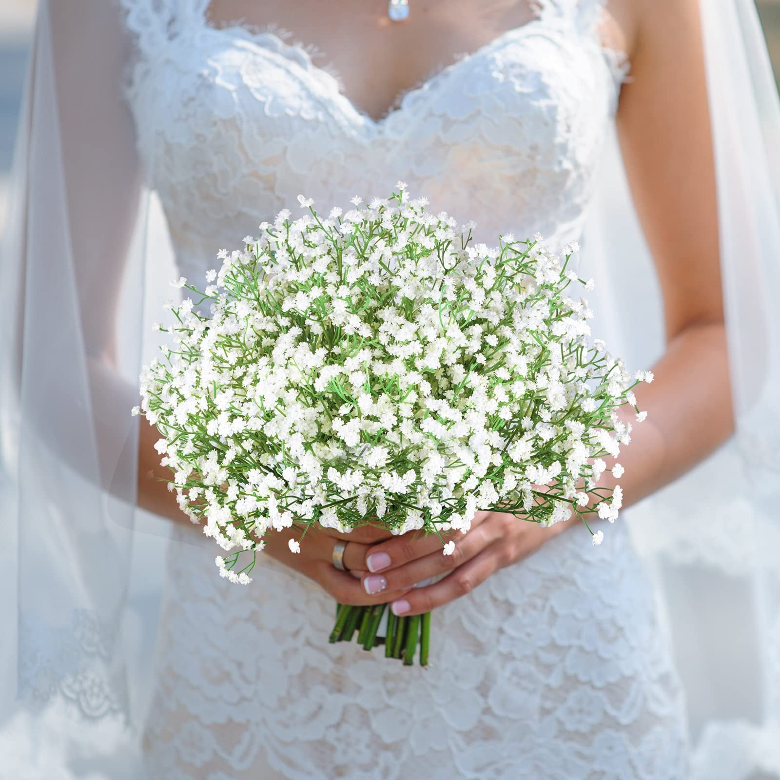 Bride holding a bouquet of white artificial baby's breath flowers with green stems.