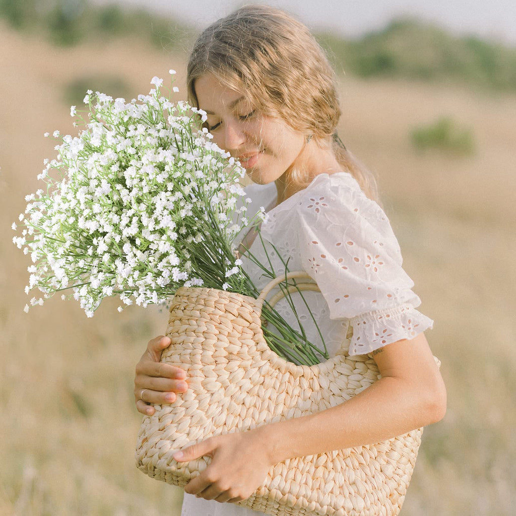 Young woman holding a woven basket filled with white baby's breath flowers, smelling them in a field.