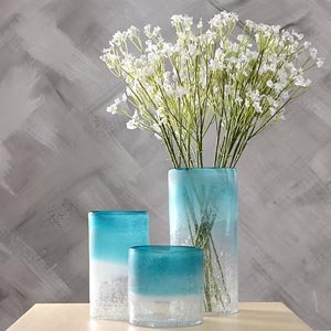 Three blue gradient glass vases with white artificial baby's breath flowers against a textured gray background.