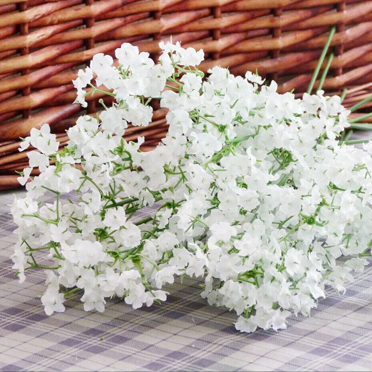 A bouquet of artificial white baby's breath flowers with green stems, arranged on a checkered cloth with a woven basket in the background.