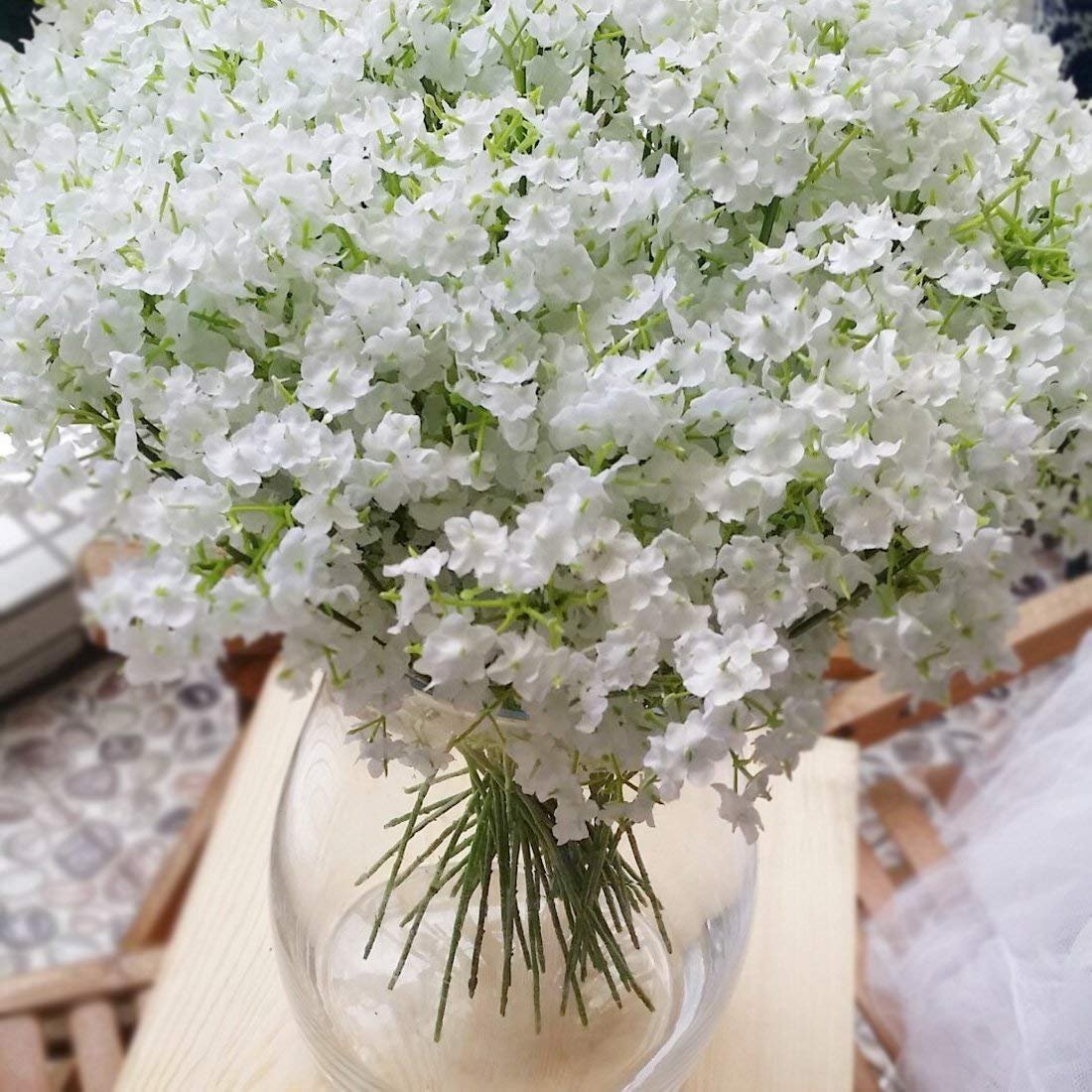 Close-up of a bouquet of artificial white baby's breath flowers in a clear glass vase, stems visible at the bottom.