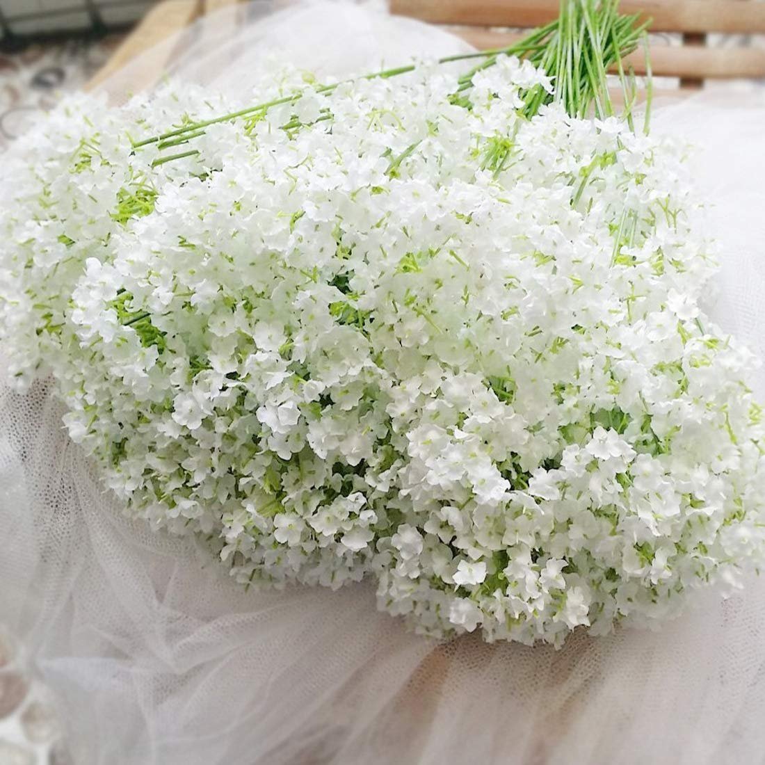 Bouquet of artificial white baby's breath flowers with green stems, laid on white tulle fabric.