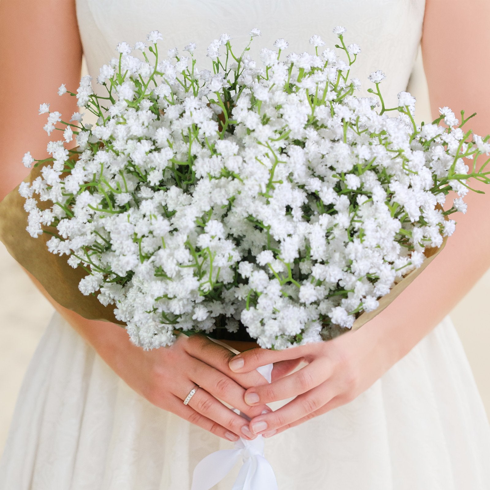 Bride holding a bouquet of white artificial baby's breath flowers wrapped in brown paper, with a white ribbon tied around the stems.