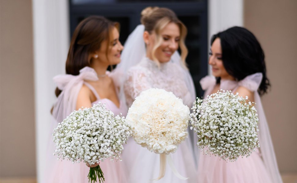 Bride and bridesmaids holding bouquets of white baby's breath flowers and one larger white flower bouquet.