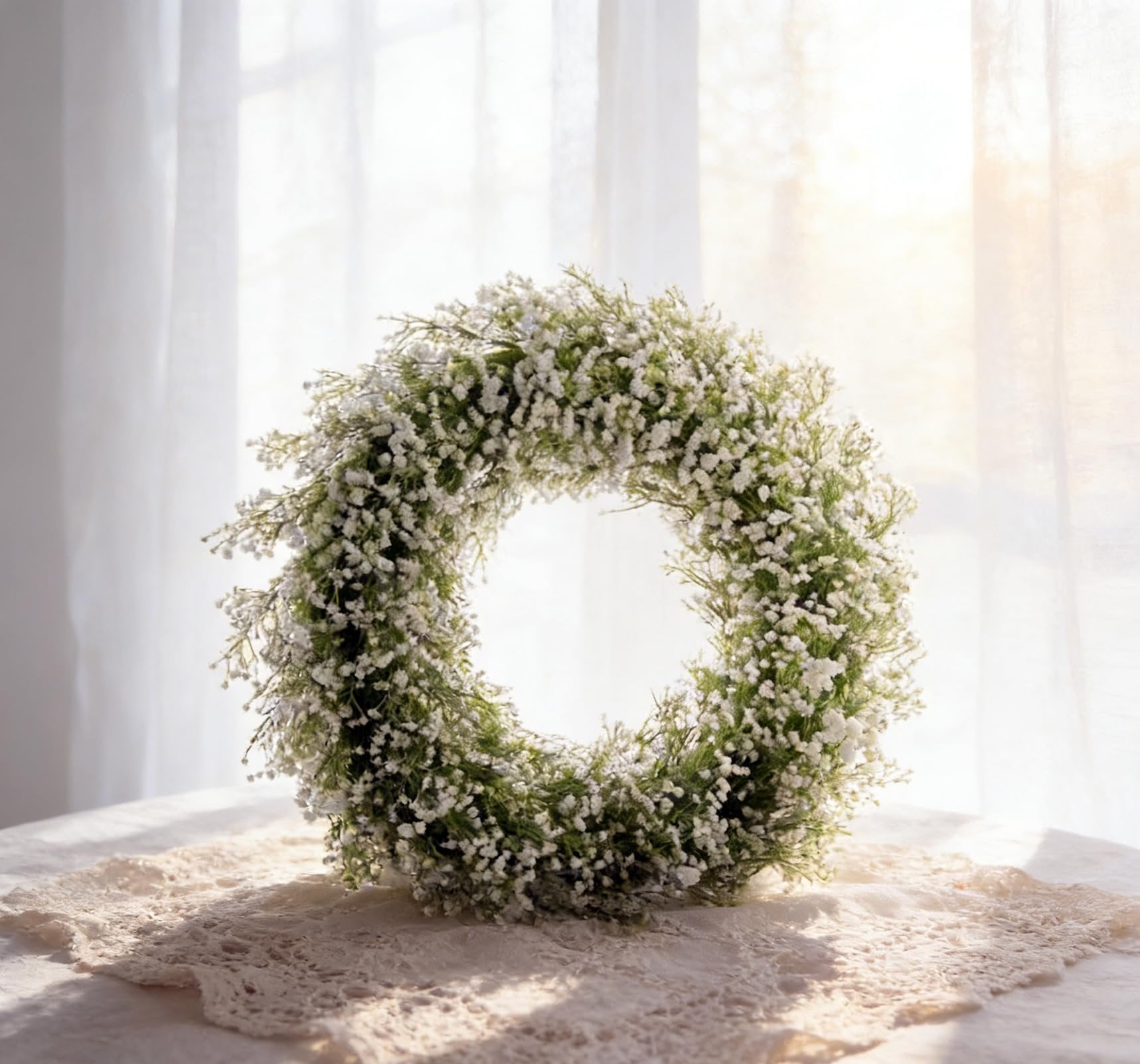 White artificial baby's breath flower wreath on a lace runner with sheer curtains in the background