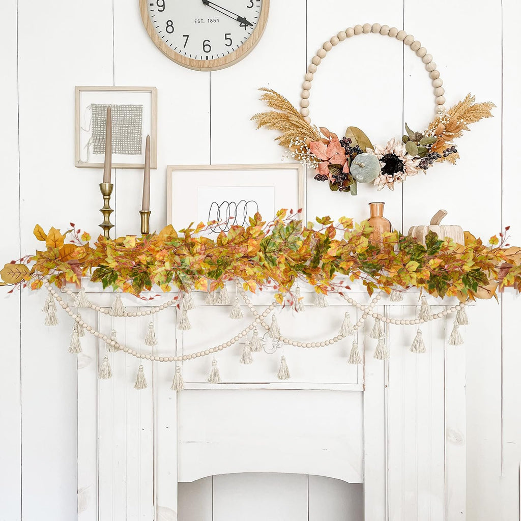 Artificial fall maple leaf garland draped over a white fireplace mantel with a beaded tassel garland below.