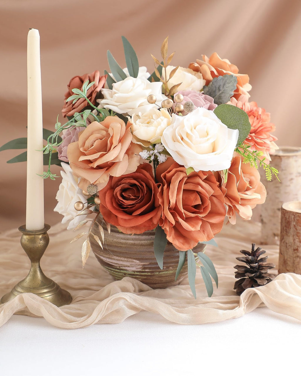 Artificial flower arrangement in a vase with a candle and pinecone, featuring terracotta dahlias, champagne peonies, amber roses, and eucalyptus leaves.