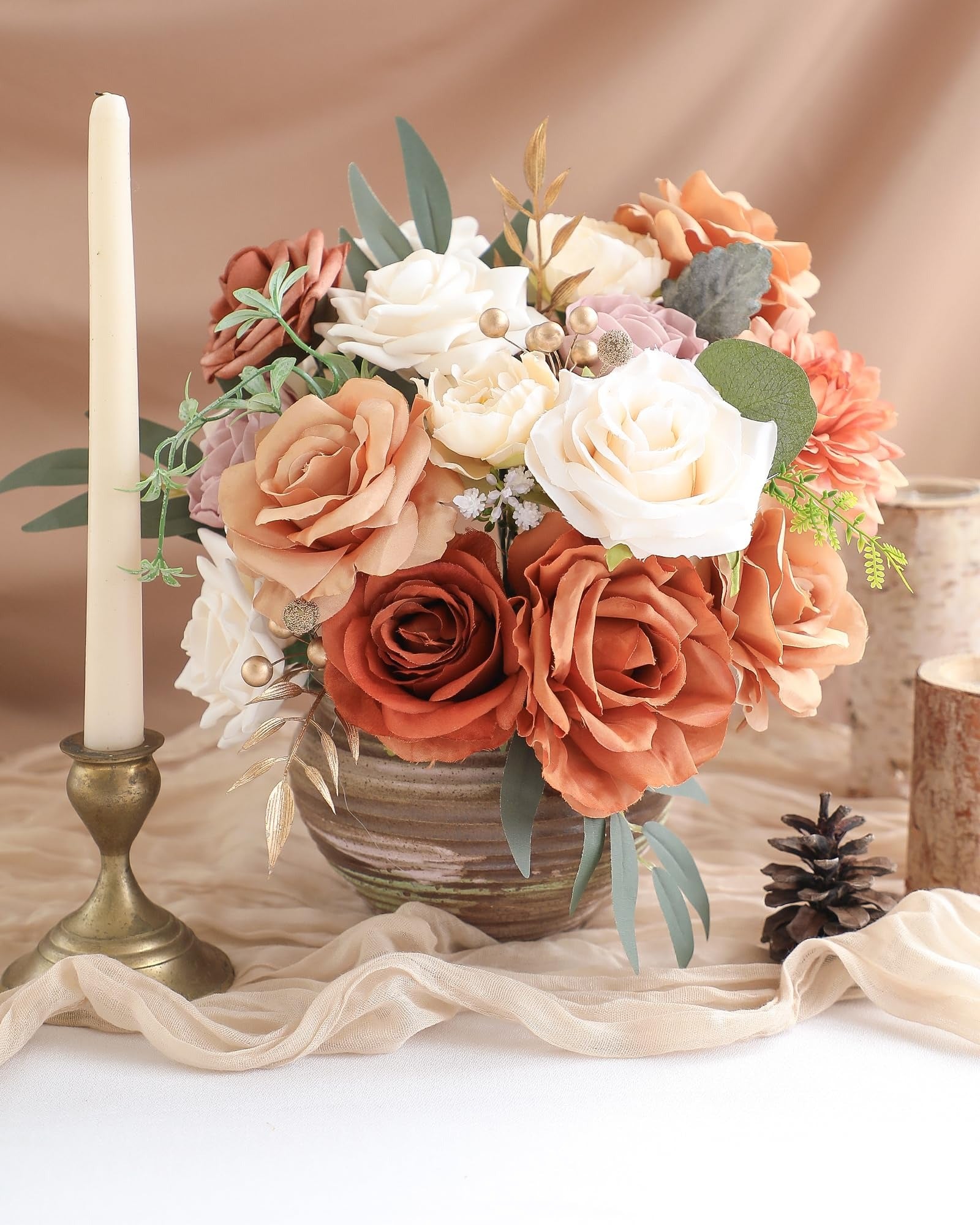 Artificial flower arrangement in a vase with a candle and pinecone, featuring terracotta dahlias, champagne peonies, amber roses, and eucalyptus leaves.