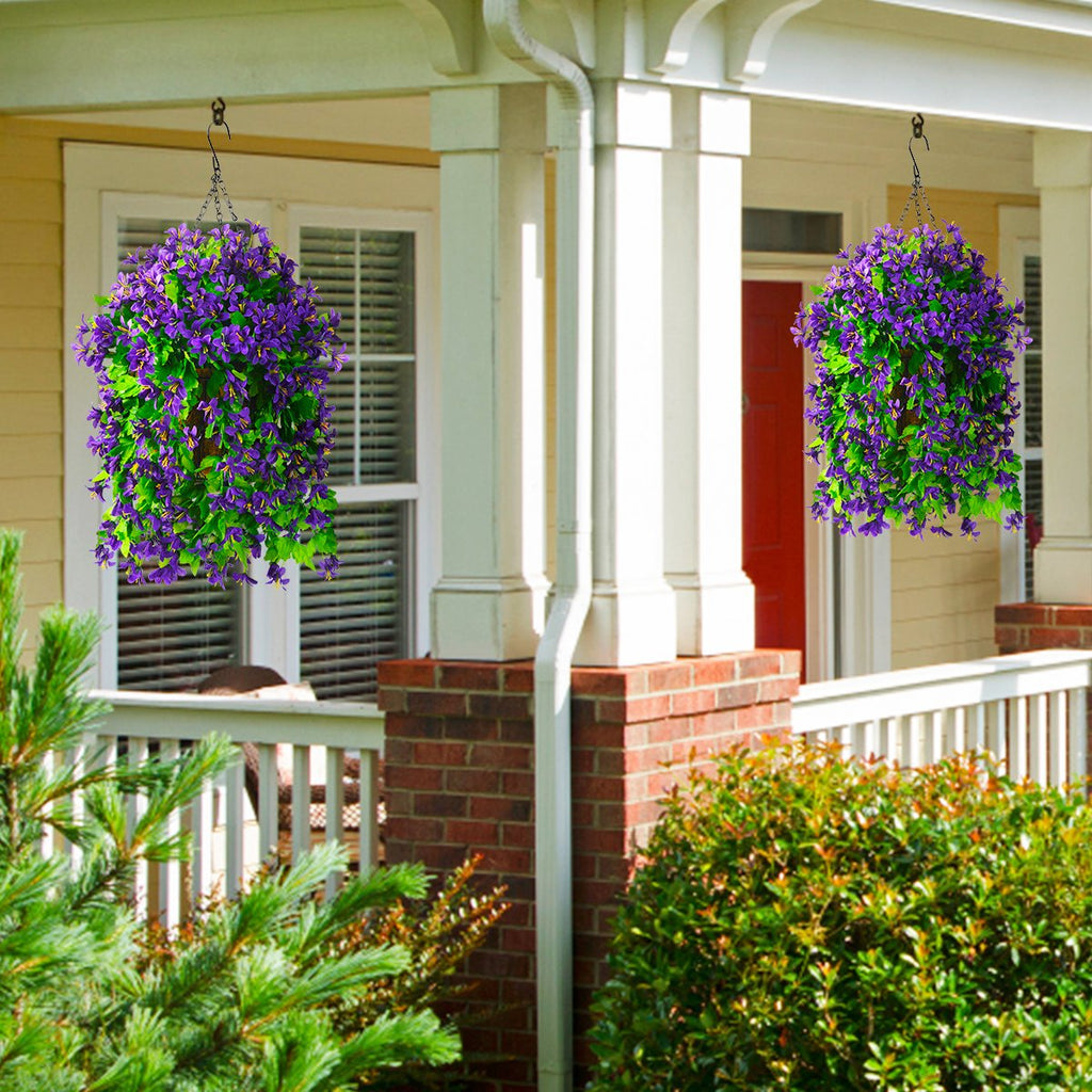 Two hanging baskets filled with artificial purple flowers and green foliage, suspended from a porch.