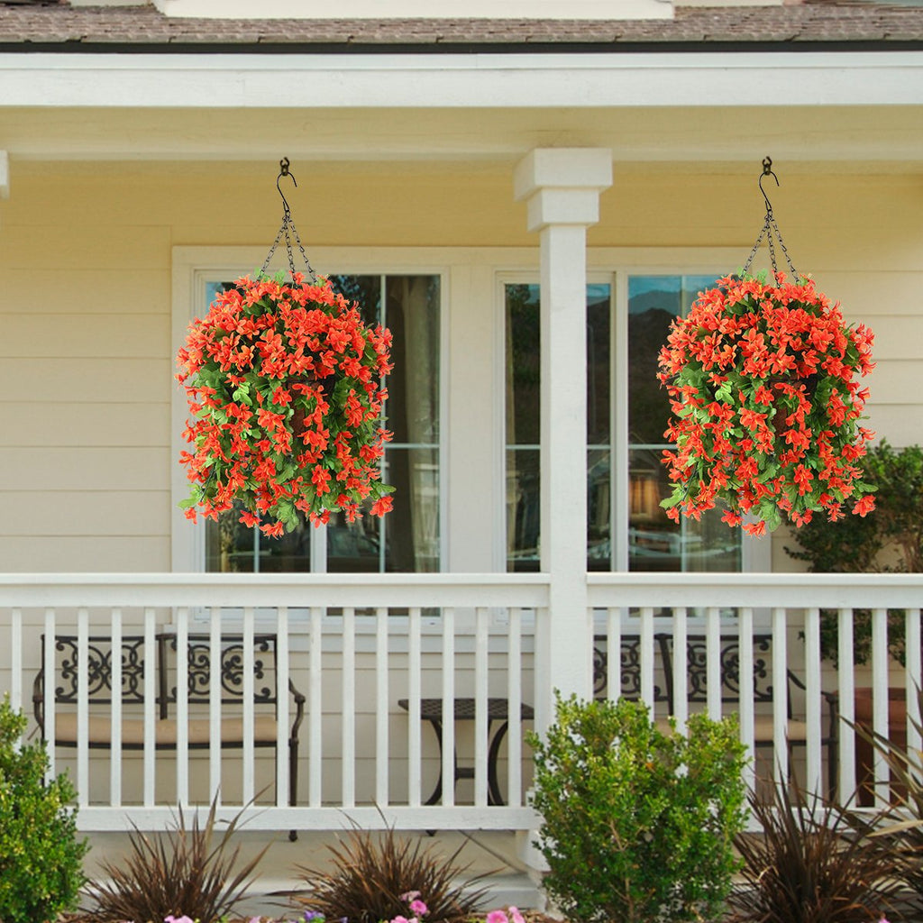 Two hanging baskets filled with vibrant orange artificial flowers and green foliage, suspended from a porch ceiling.
