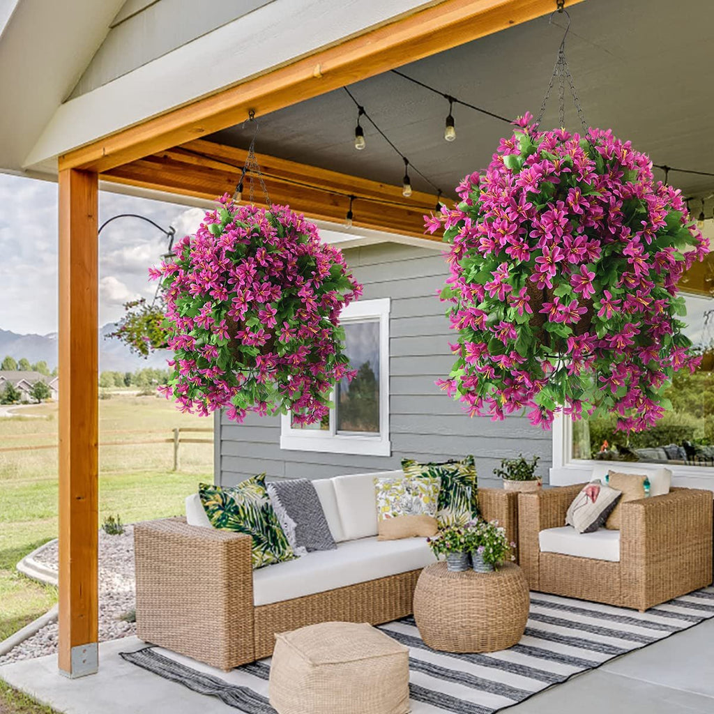 Two hanging baskets filled with vibrant pink artificial flowers and green leaves, suspended from a porch ceiling.