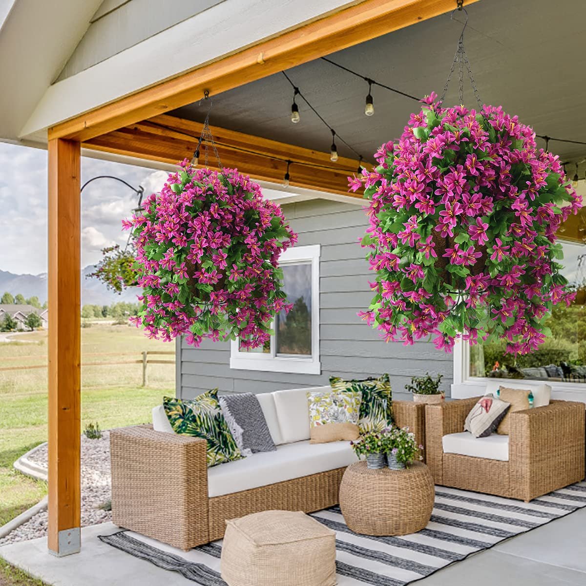 Two hanging baskets filled with vibrant pink artificial flowers and green leaves, suspended from a porch ceiling.
