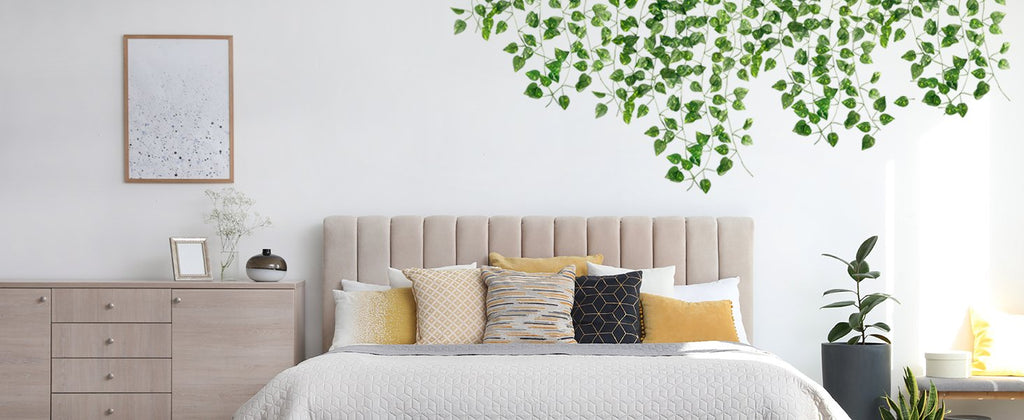 Artificial ivy vines draped over a bed in a bedroom setting, showing green silk leaves and plastic stems.