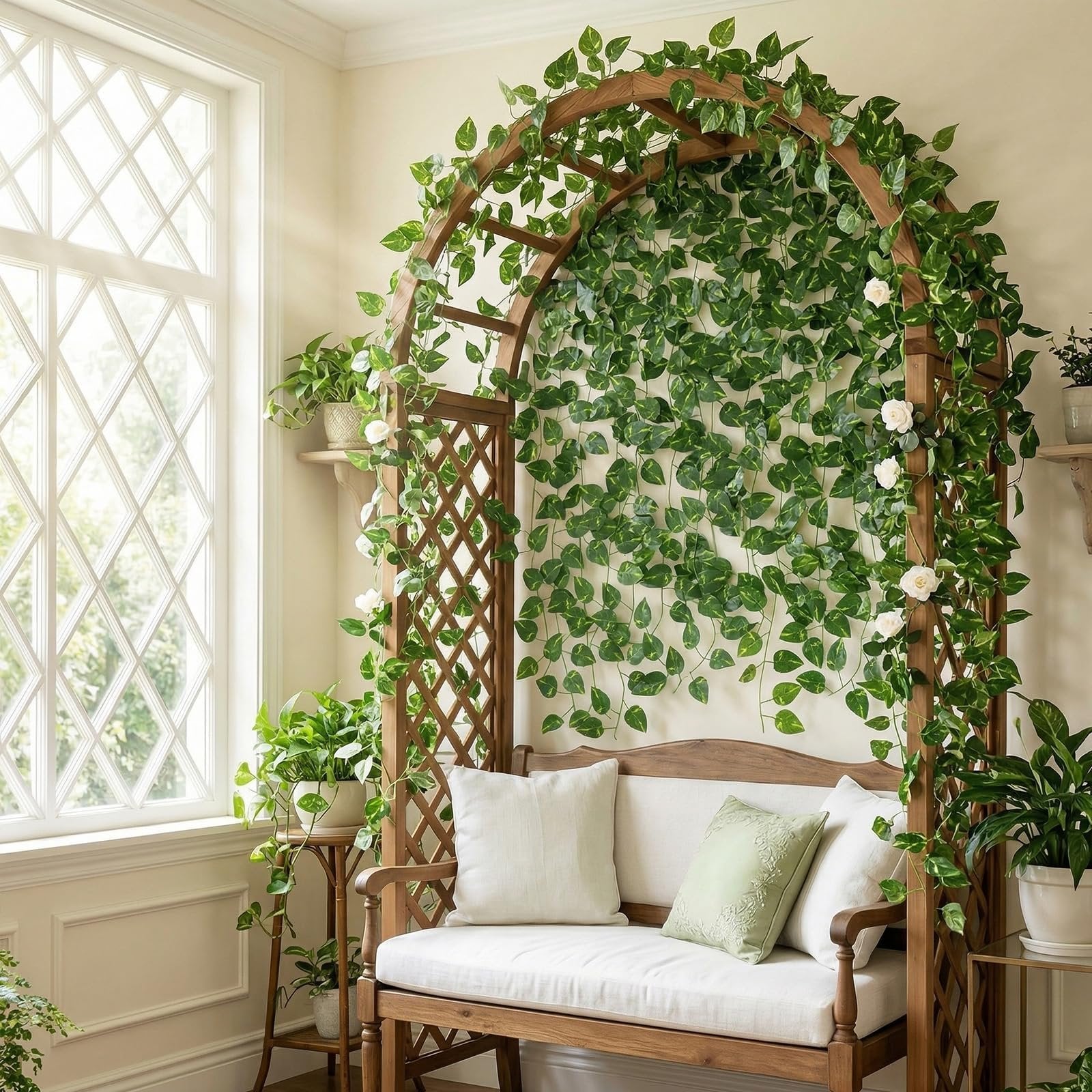 Artificial ivy vines with white roses draped over a wooden garden arch with a bench and pillows