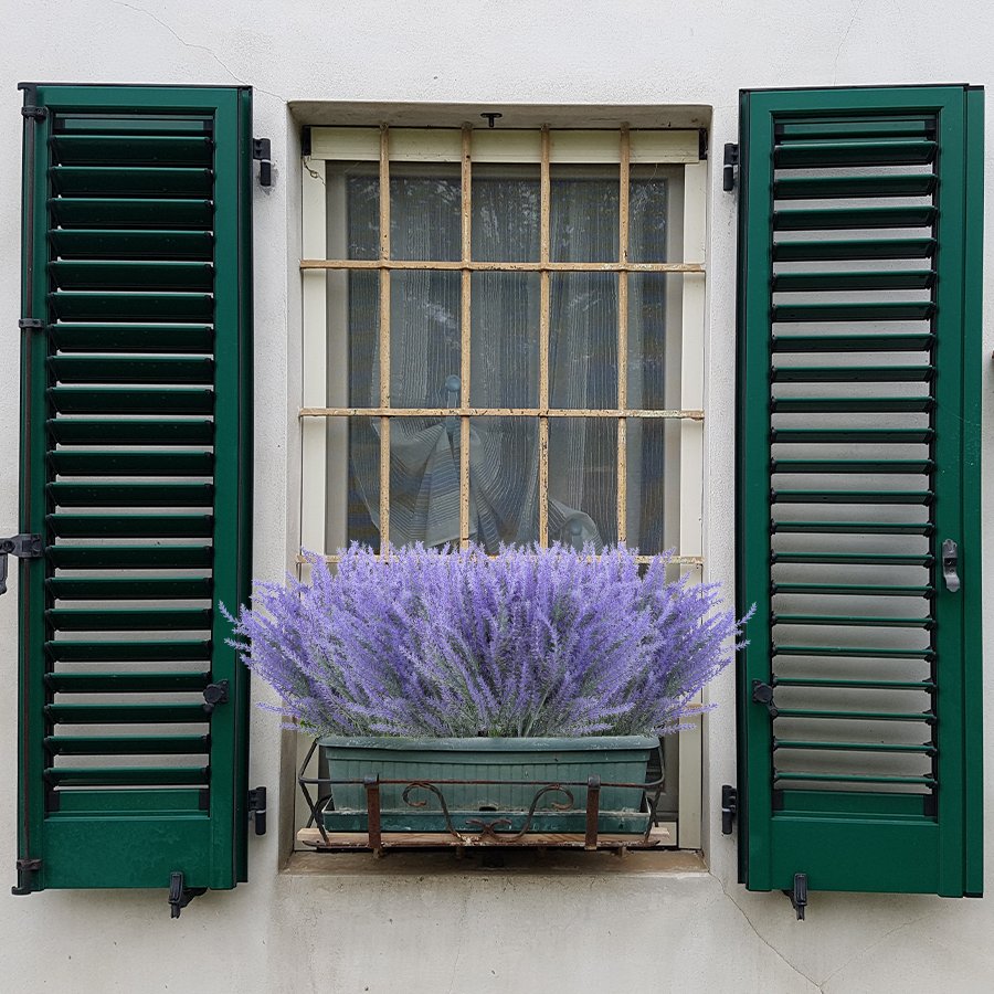 Artificial lavender bundles in a window planter box with green shutters.