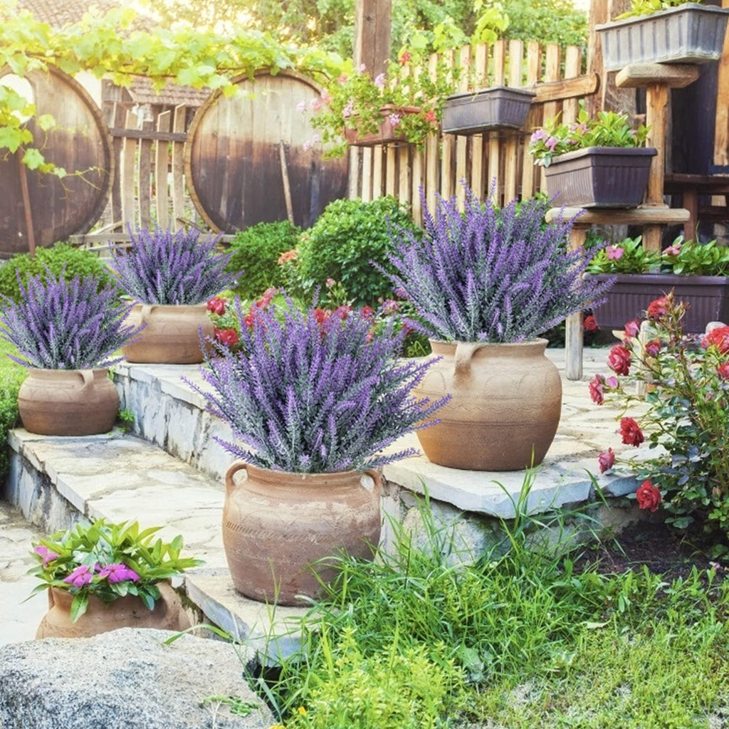 Artificial lavender bundles in terracotta pots on stone steps with wooden barrels and greenery in the background.