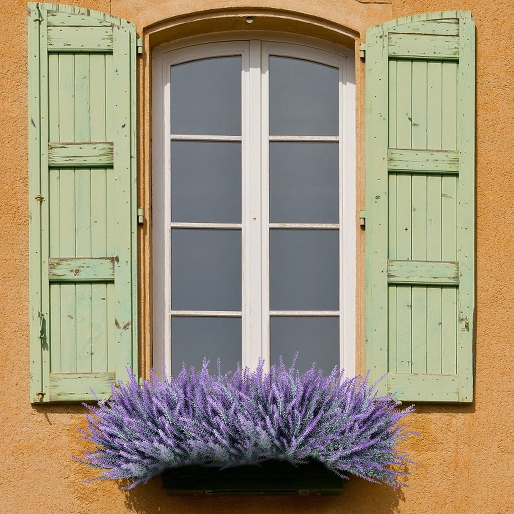 Artificial lavender bundles in a window box below a white-paned window with green shutters.
