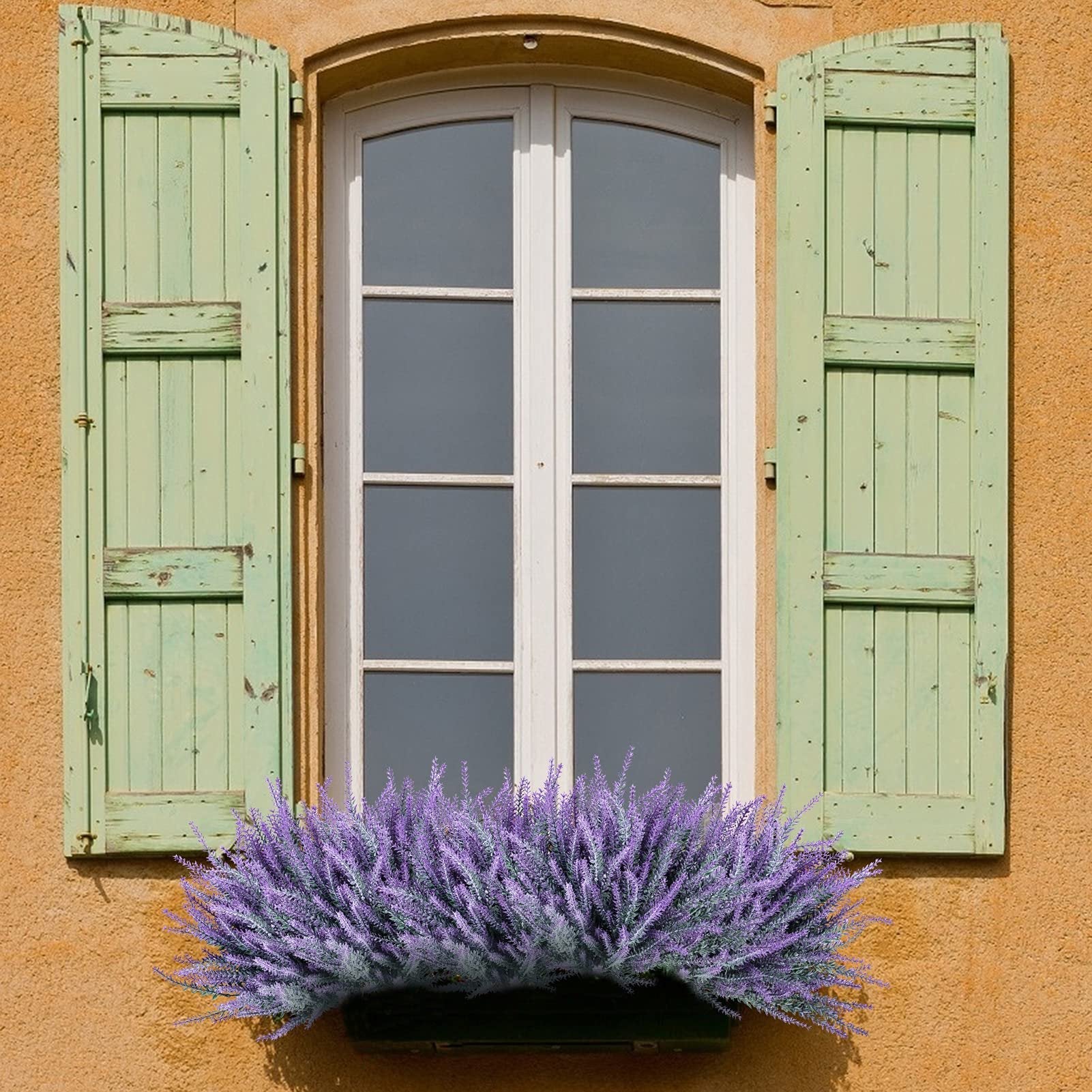 Artificial lavender bundles in a window box below a white-paned window with green shutters.