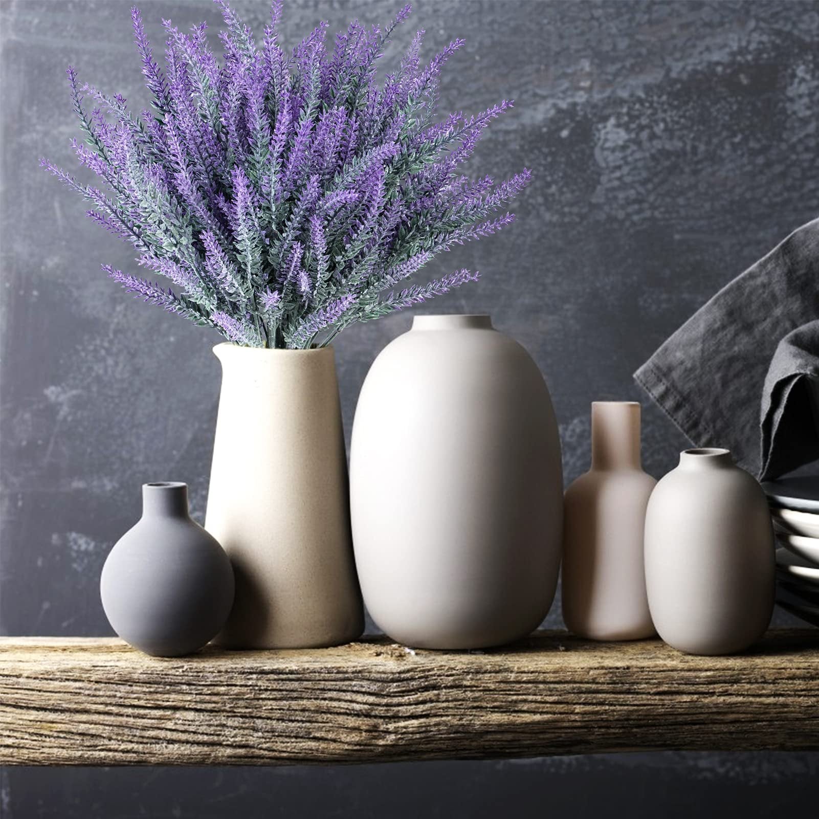 Artificial lavender bundles in vases on a rustic wooden shelf with a dark textured background.