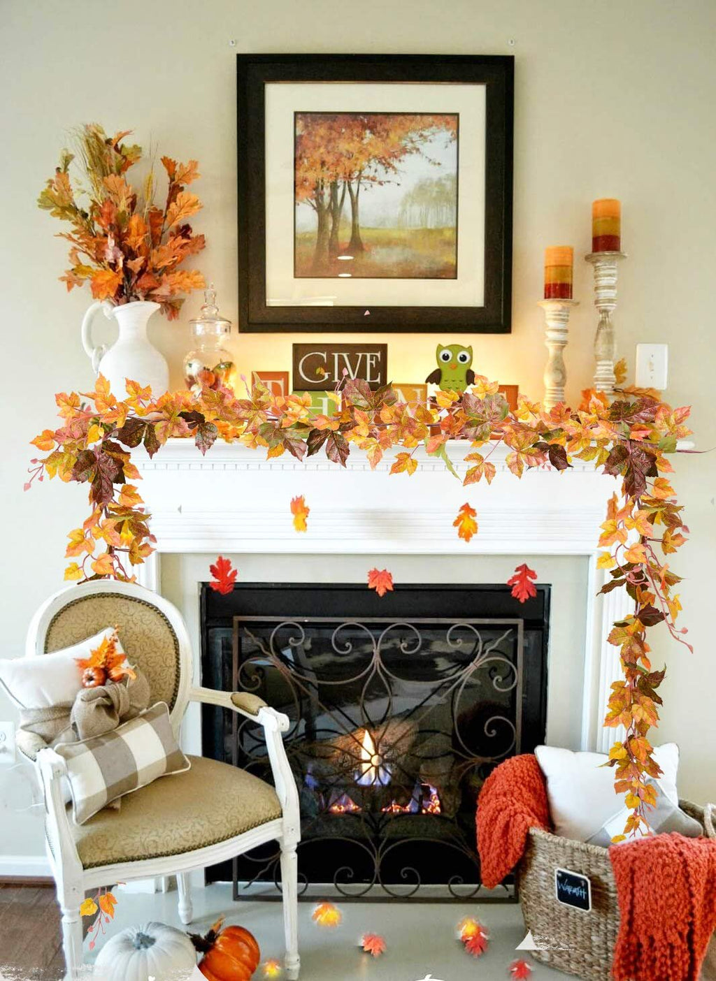 Artificial maple leaf garland draped over a fireplace mantel with a painting and candles above.