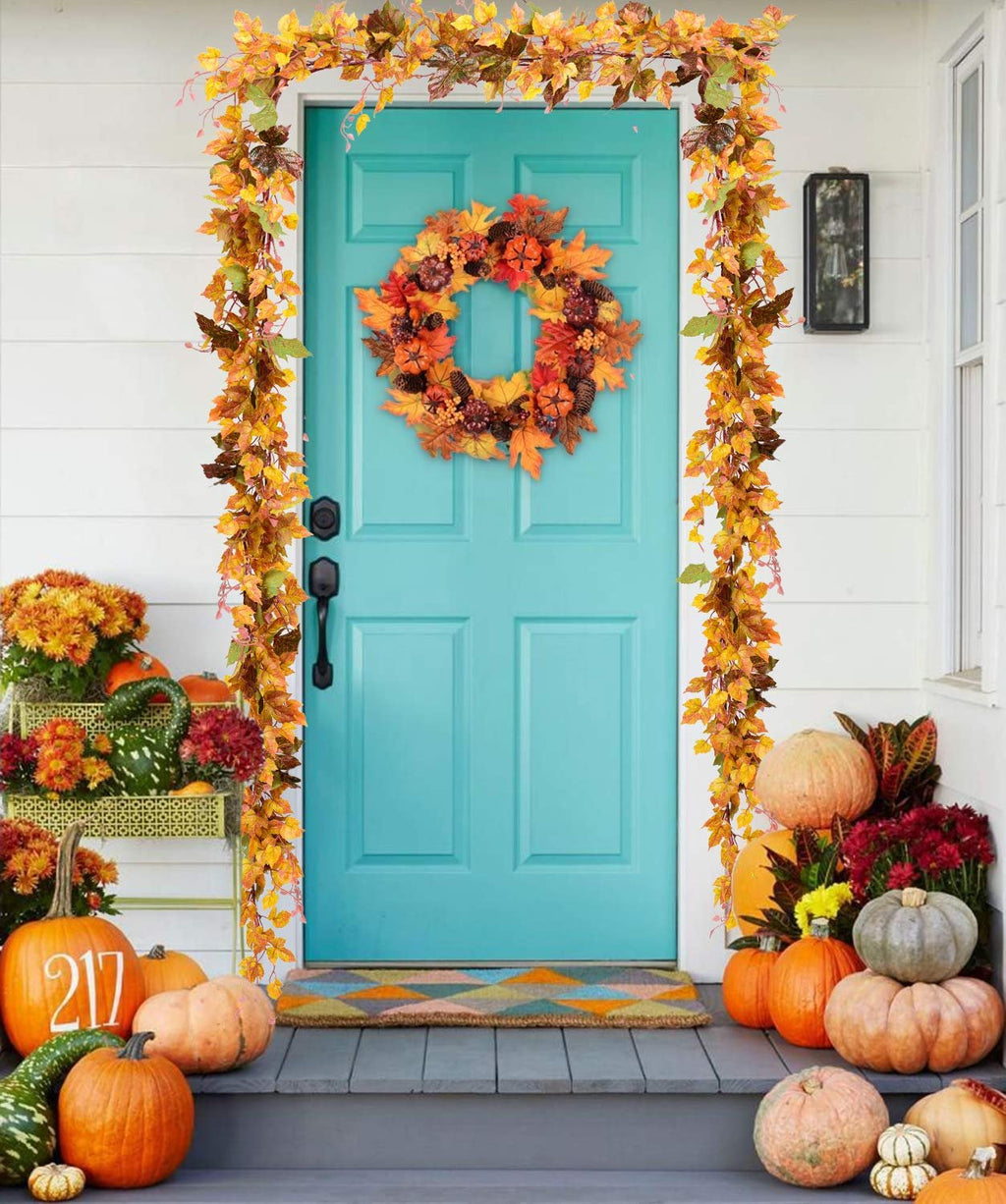 Autumn maple leaf garland and wreath decorating a teal front door with pumpkins and fall flowers on the porch.