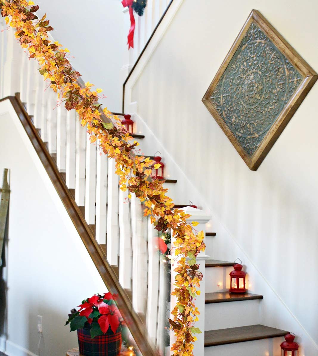 Artificial maple leaf garland draped along a staircase railing with red lanterns on steps.